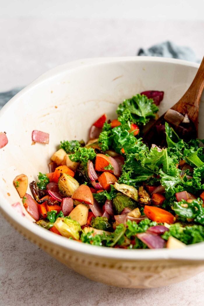 Roasted vegetable kale salad in a large mixing bowl with a wooden spoon.