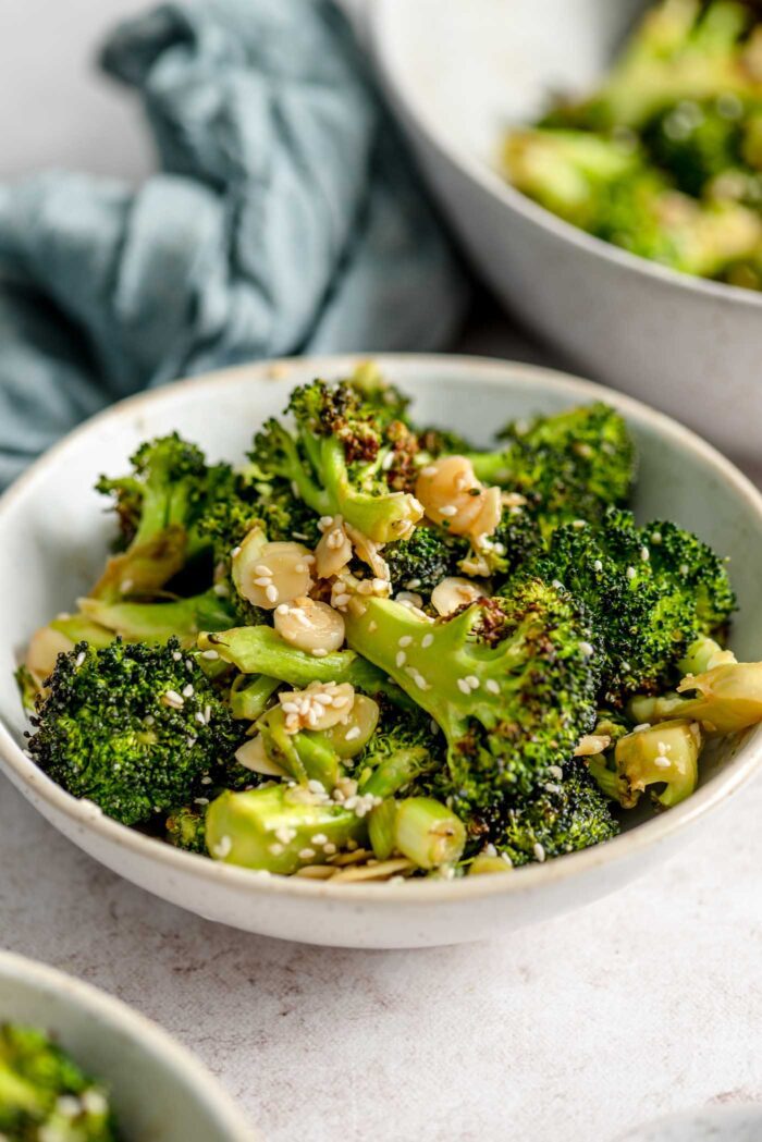 Bowl of roasted broccoli salad with slivered almonds and green onions.