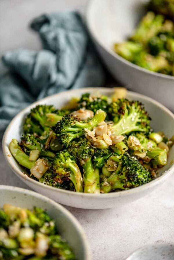 Bowl of roasted broccoli salad with slivered almonds and green onions.