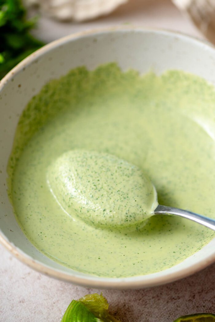 Spoon scooping creamy green tahini sauce in a bowl.