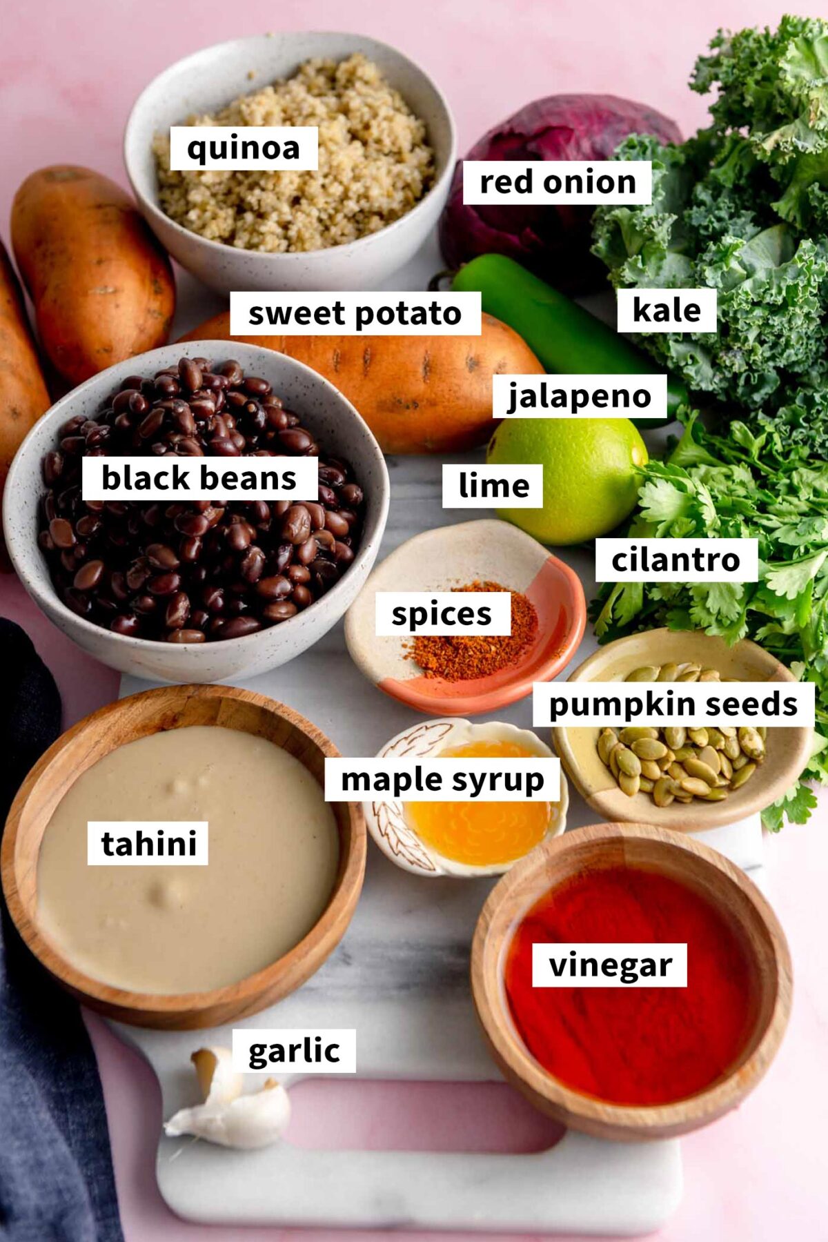 All the ingredients for making a sweet potato quinoa black bean bowl with kale gathered in various bowls on a marble cutting board.