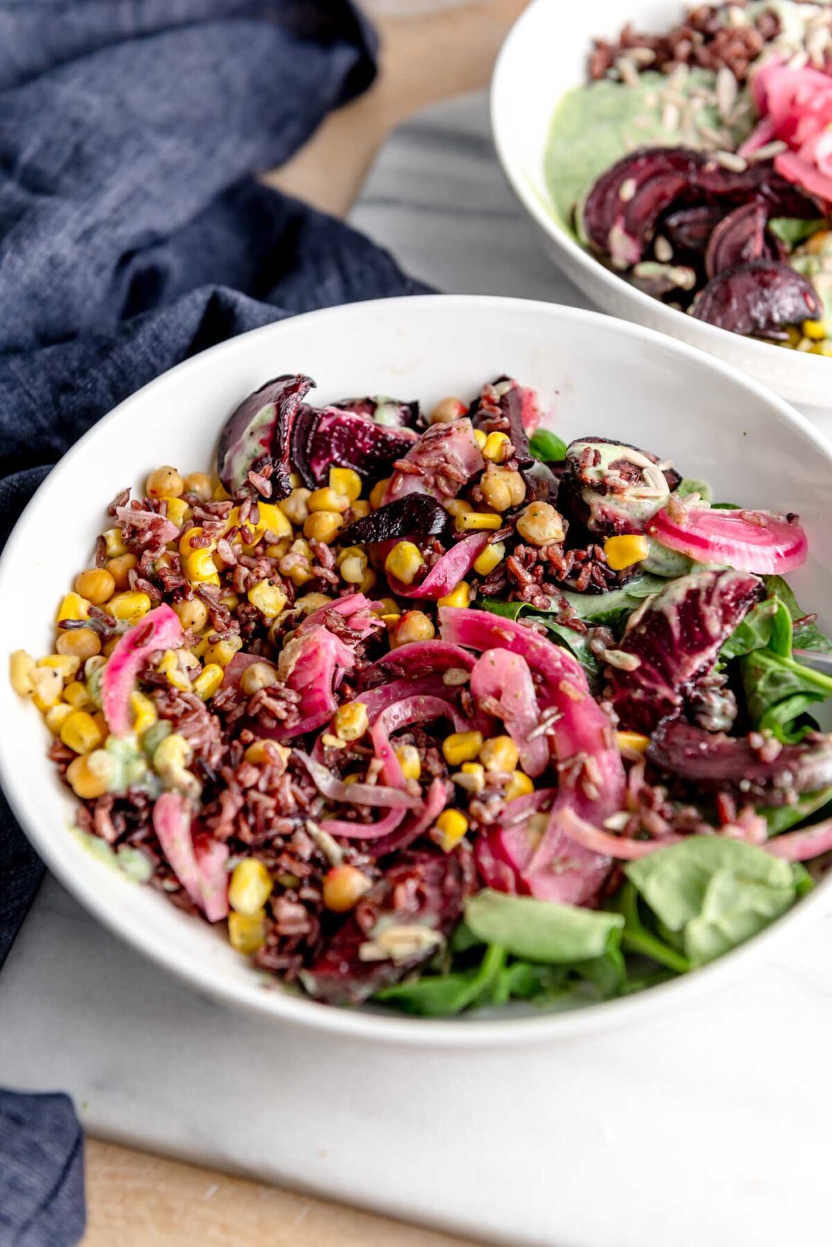 Wild rice salad with pickled onion, corn and chickpeas in a bowl sitting on a marble cutting board.