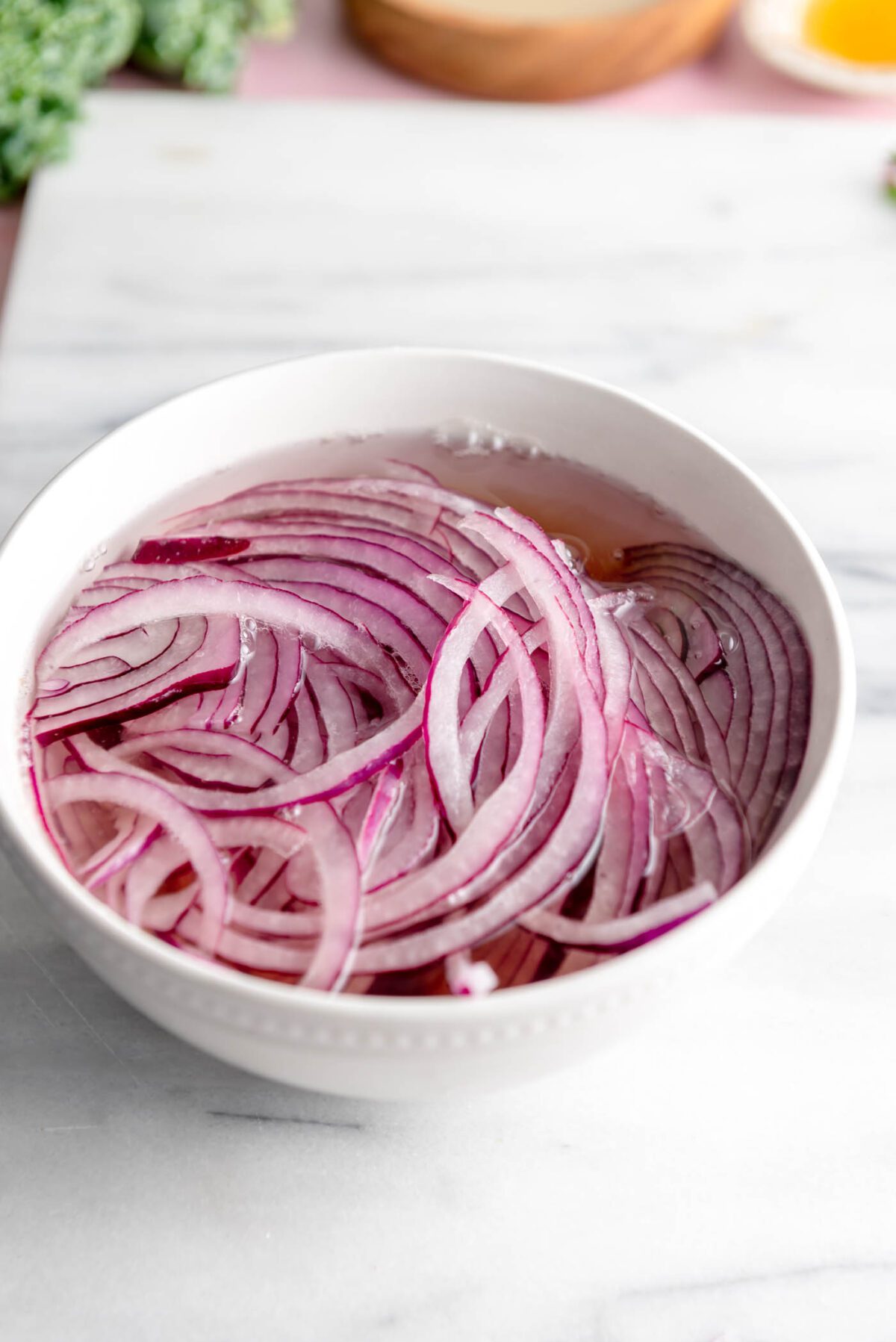 Thinly sliced red onion in water in a bowl.