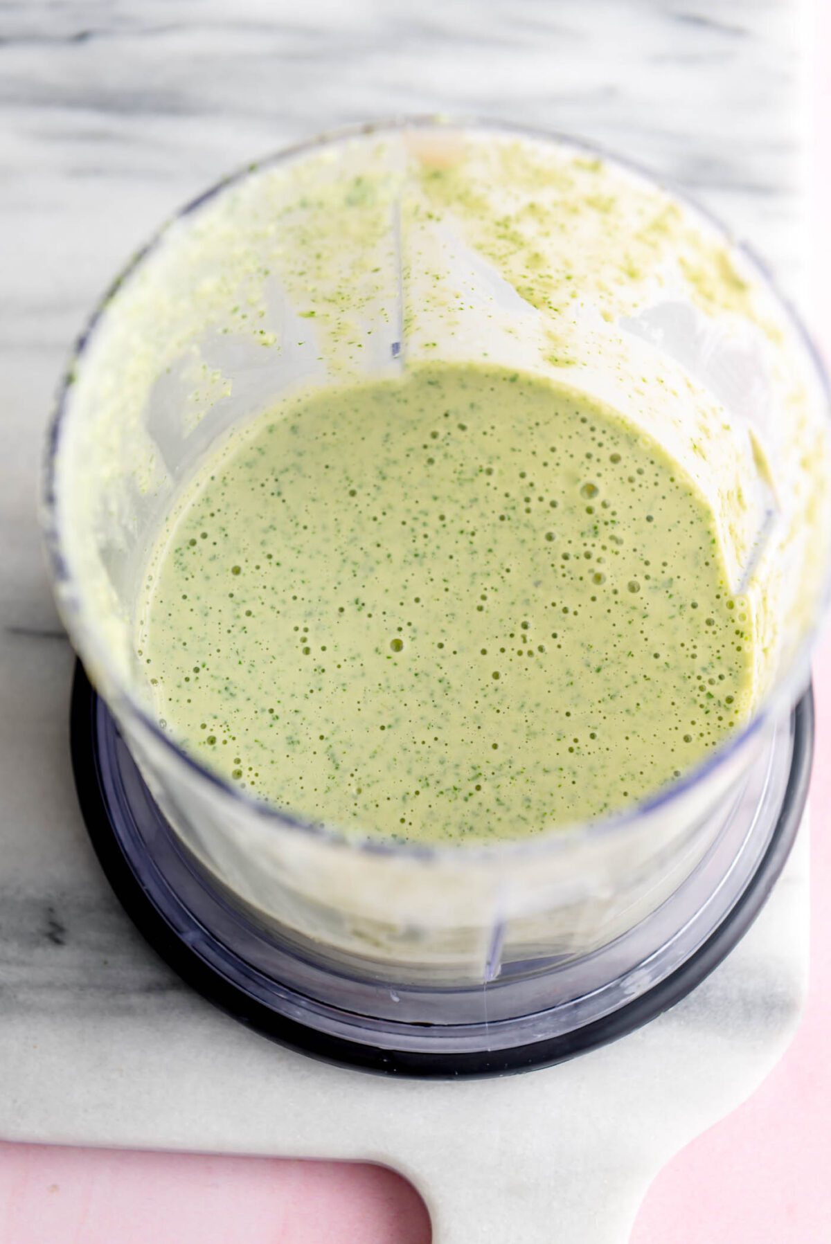 Green creamy tahini dressing in a small food processor container.