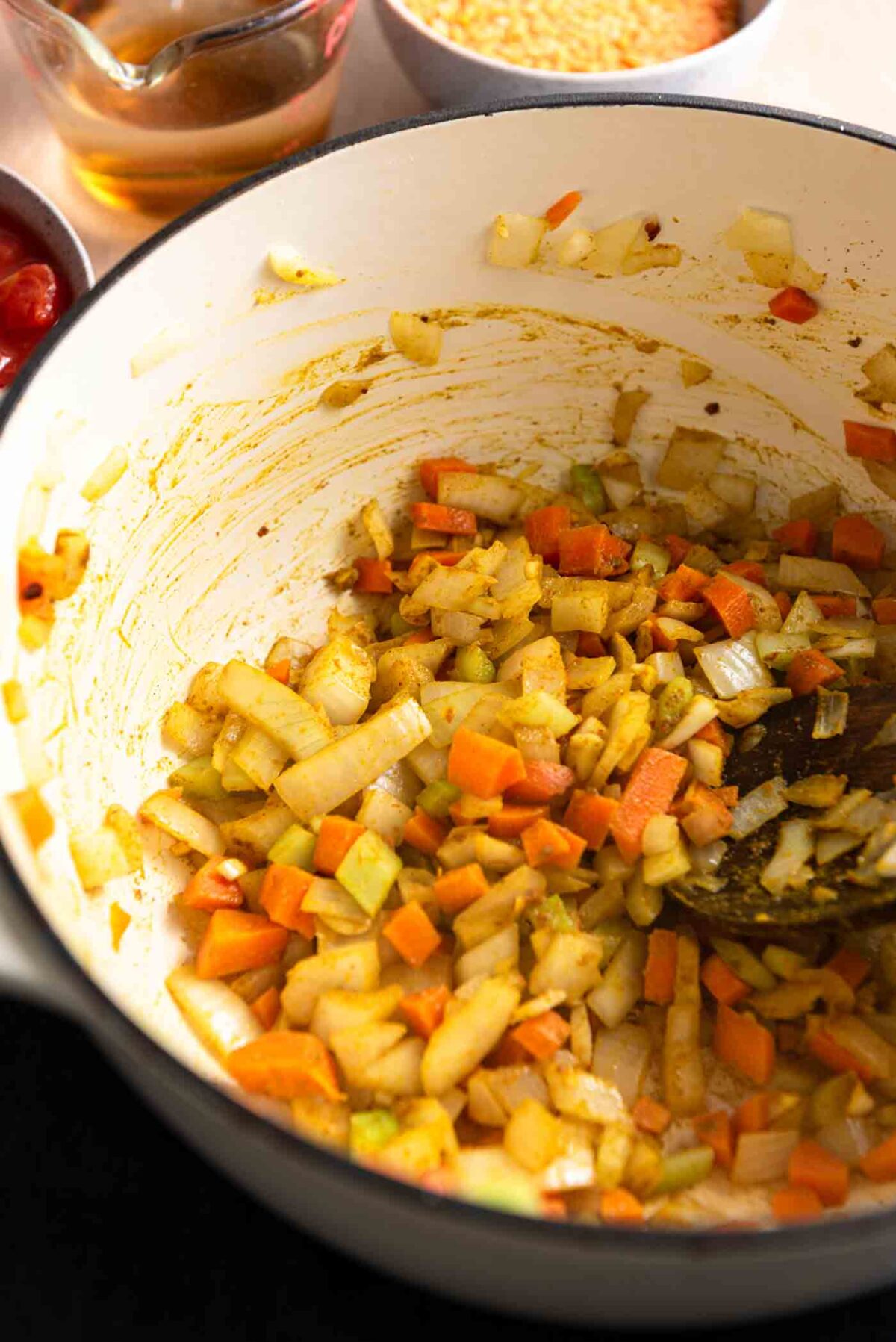 Carrot, onion, garlic and celery cooking in curry spices in a soup pot.