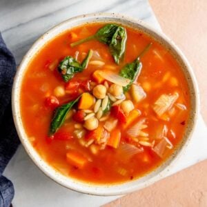 Bowl of tomato orzo spinach soup on a marble cutting board.