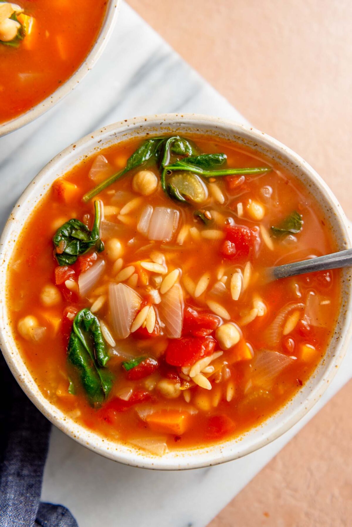 Bowl of tomato orzo spinach soup on a marble cutting board.