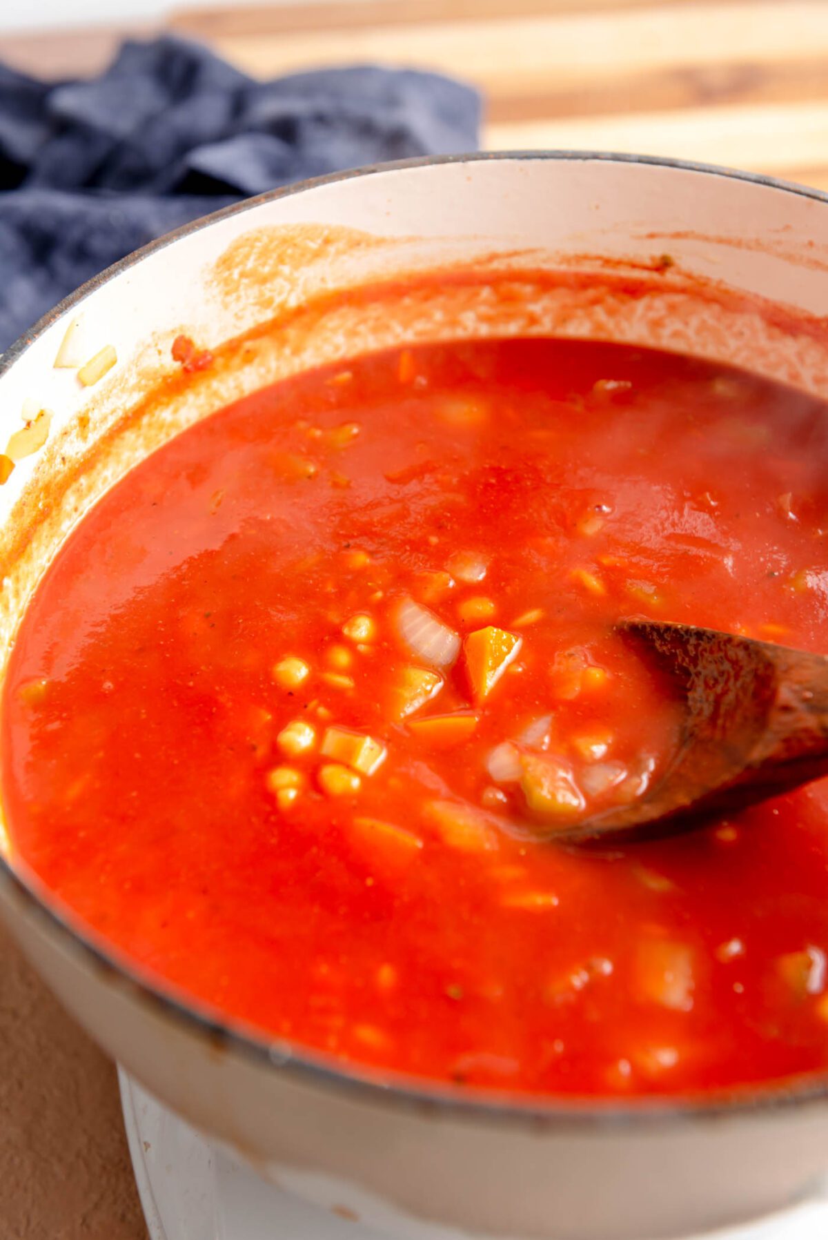 Chickpeas and orzo cooking in a tomato broth in a soup pot with a wooden spoon.