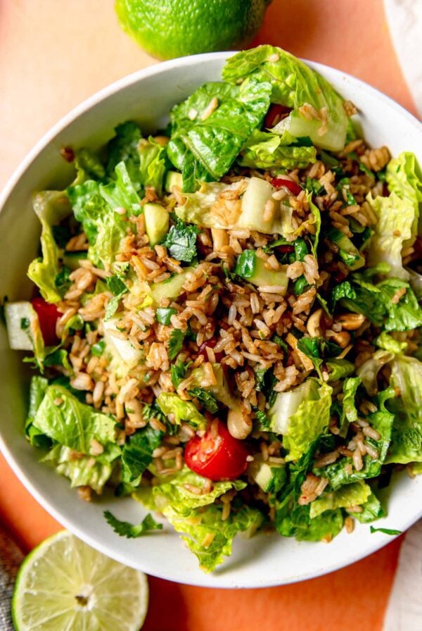 Crispy rice salad with peanuts, lettuce, tomato, cucumber and herbs in a bowl with a wedge of lime beside it.