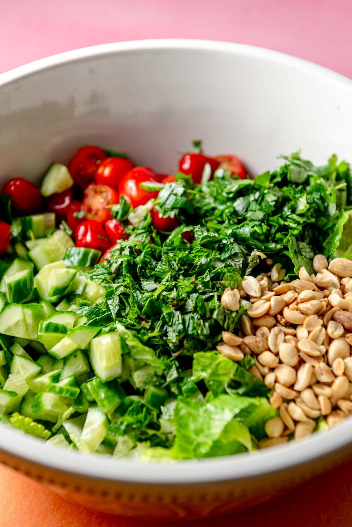 Peanuts, herbs, cucumber, tomato and lettuce in a large bowl.