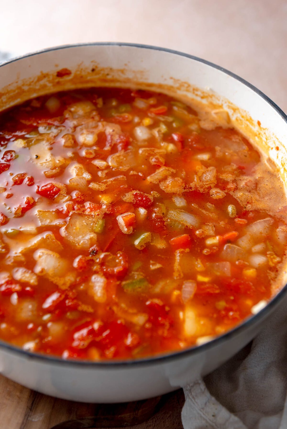 Onion, bell pepper and beans cooking in a tomato-based broth in a soup pot.