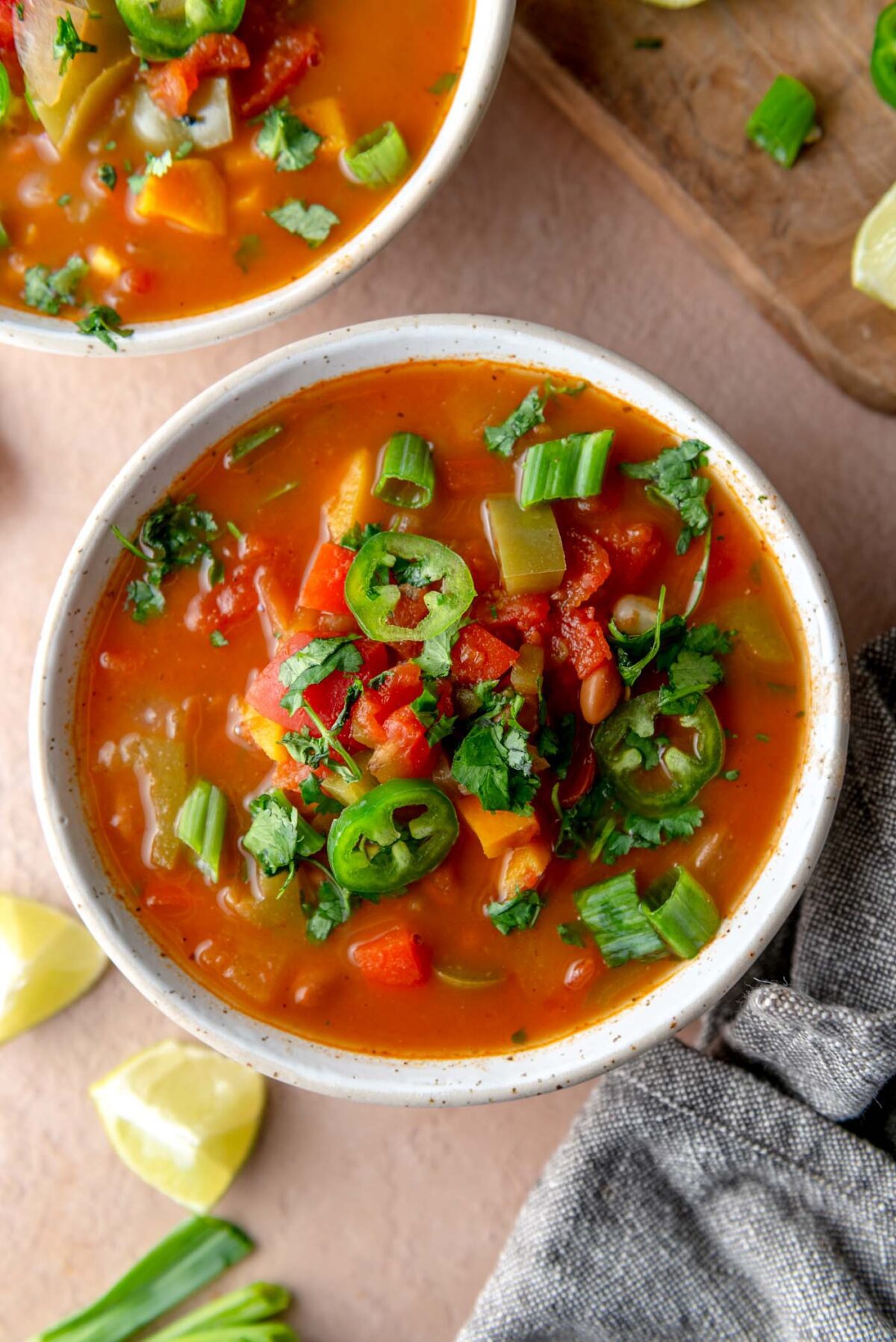 Bowl of vegetarian enchilada soup with pinto beans, sweet potato, bell peppers, topped with cilantro, green onion and jalapeno slices.