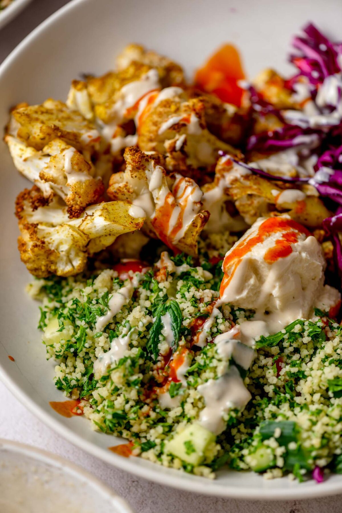 Roasted spiced cauliflower in a bowl with tabouleh and pickled red cabbage. 