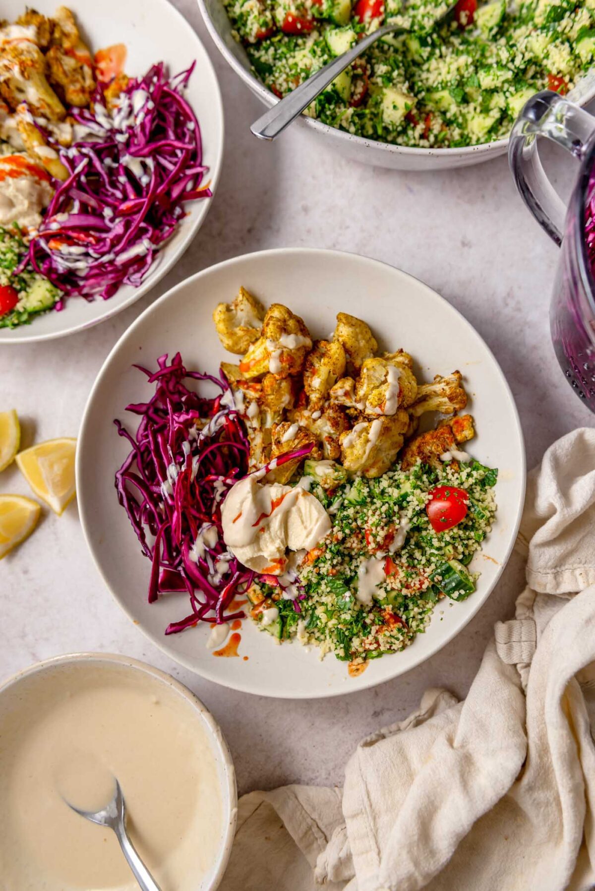 Cauliflower shawarma bowl with roasted spiced cauliflower, shredded cabbage, couscous tabouleh, hummus and tahini sauce and hot sauce drizzled over top.