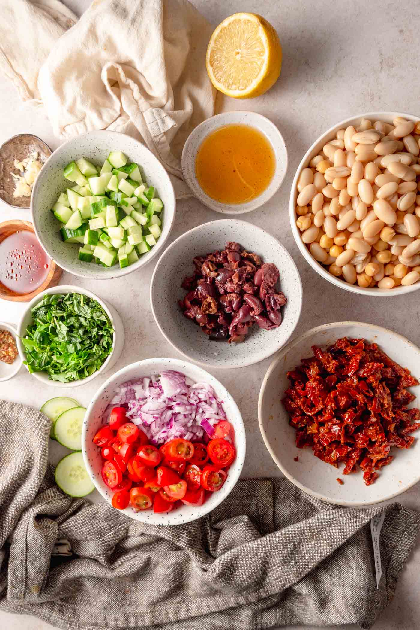 Chopped cucumber, olives, bell pepper, tomato, chickpeas, sun dried tomato in small bowls.