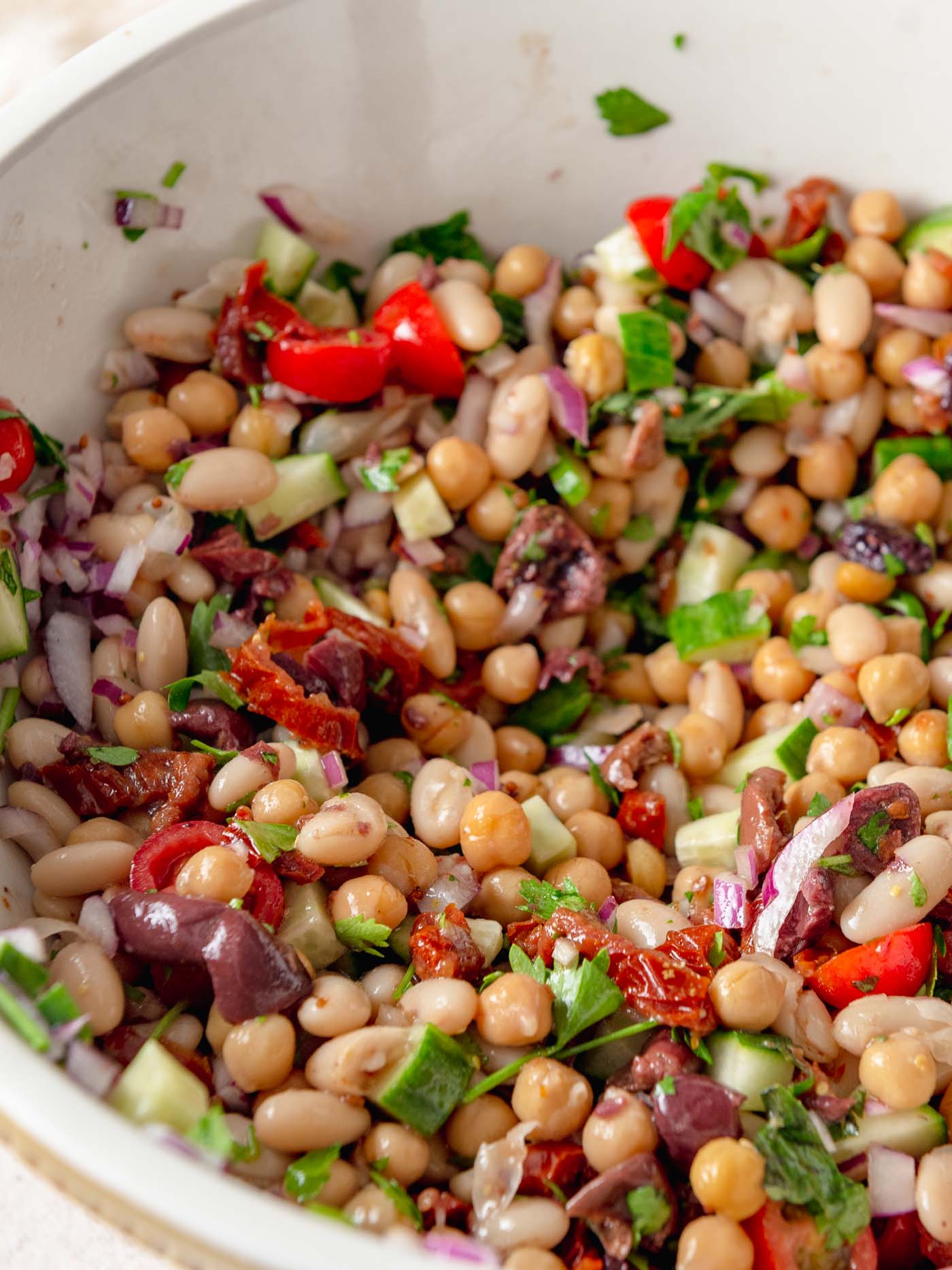 Bowl of sun dried tomato bean salad with tomato, cucumber and olives.