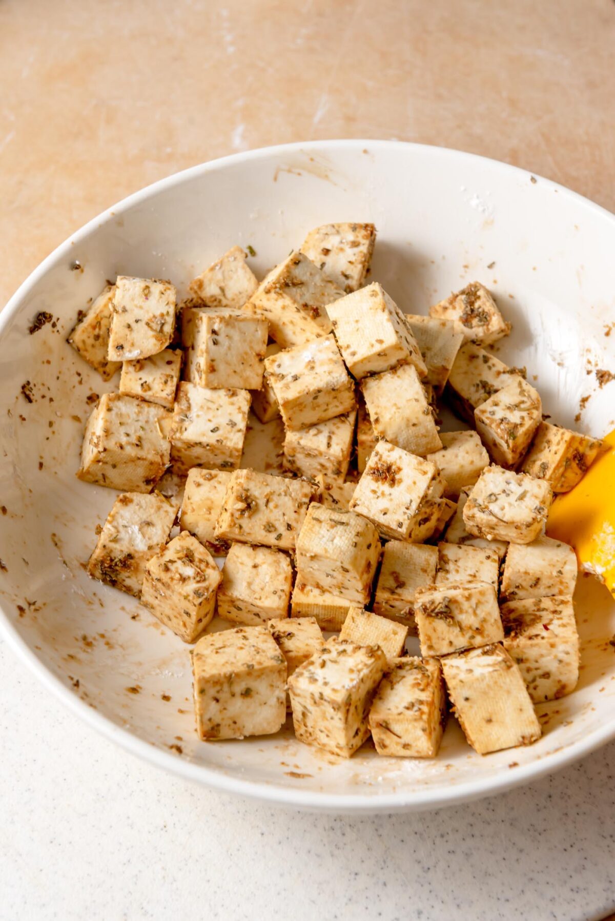 Marinated tofu cubes tossed with herbs, soy sauce, and lemon in a white bowl for Mediterranean roasted veggie bowls.