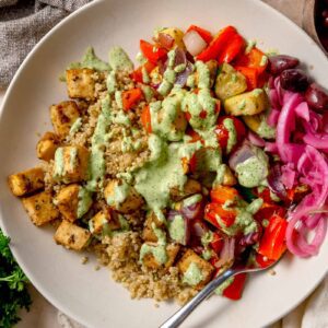 Mediterranean roasted veggie bowl with crispy lemon tofu, quinoa, roasted vegetables, and green tahini sauce.