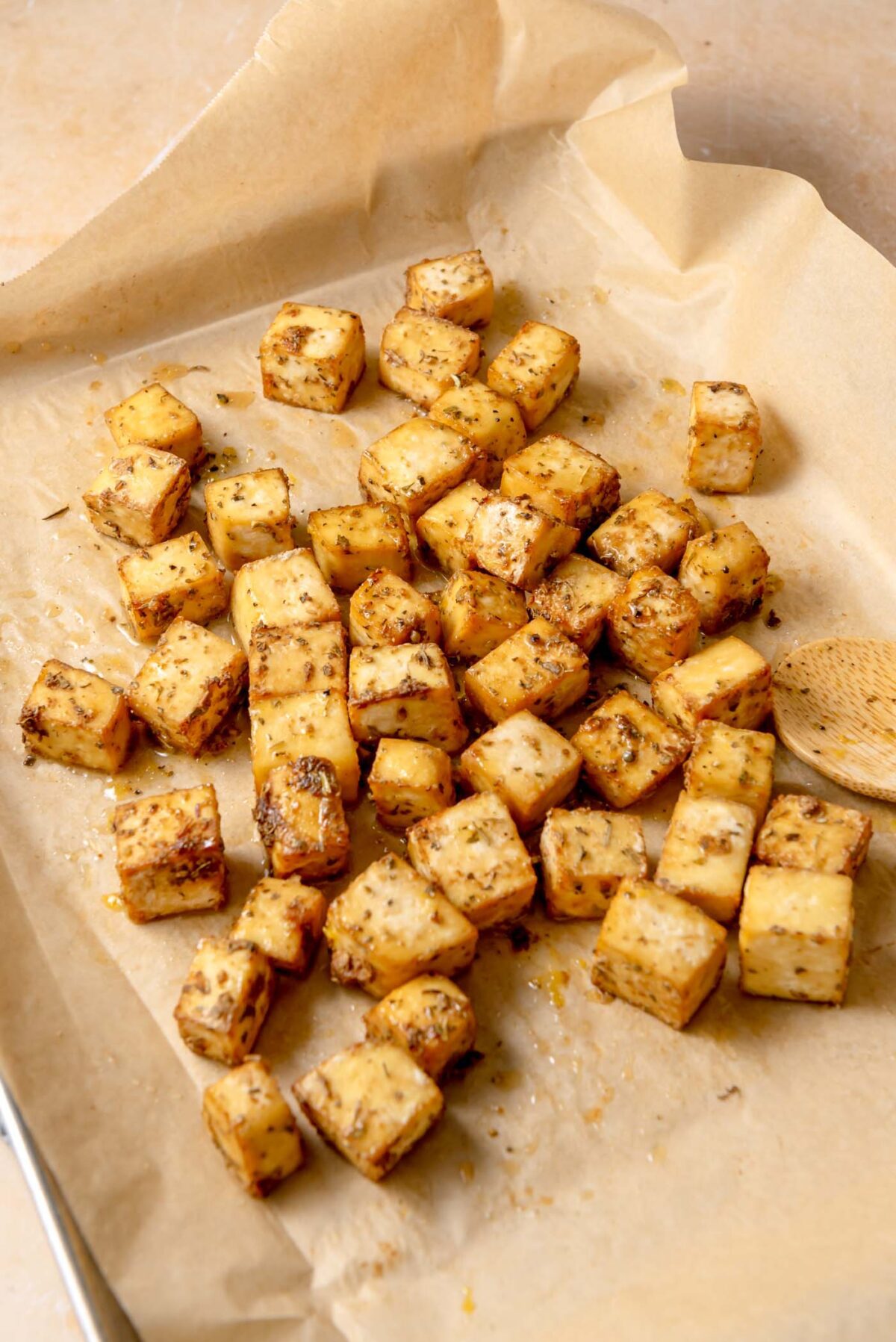 Golden baked tofu cubes with herbs cooling on a parchment-lined pan.