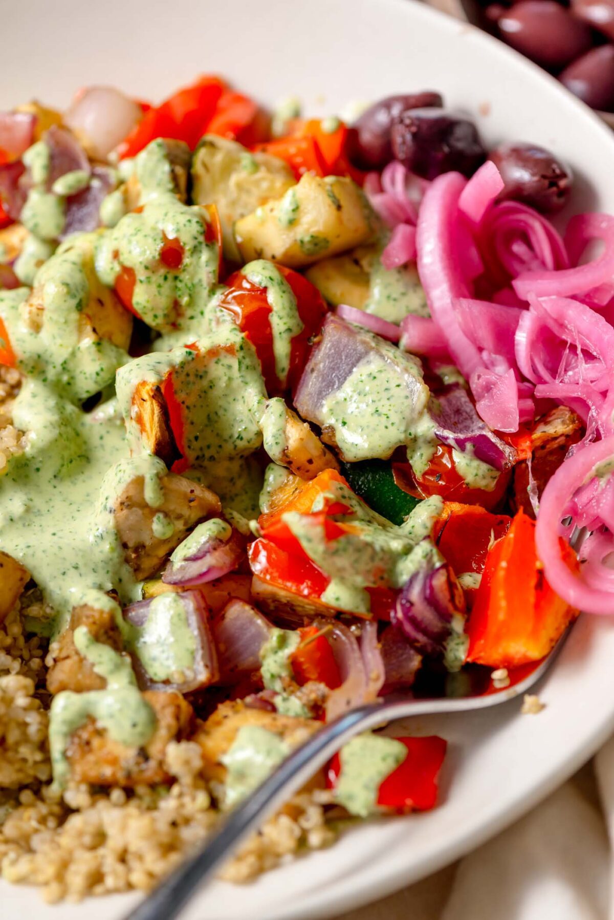 Close-up of roasted vegetables, lemon herb tofu, and tahini sauce with pickled onions and olives.