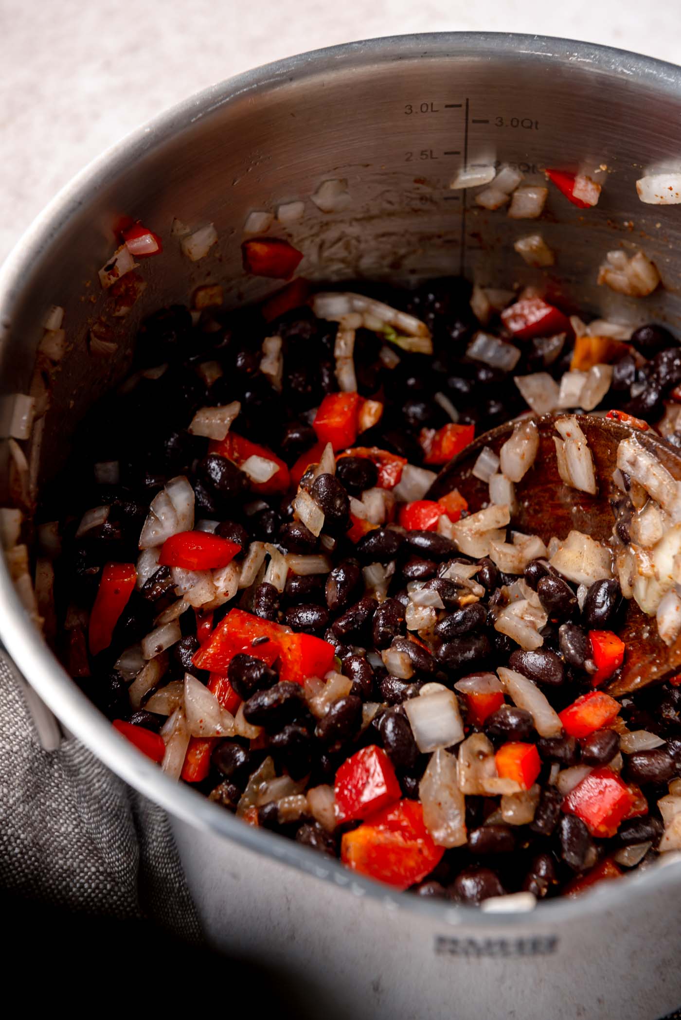 Sautéed black beans, diced onion, and red pepper cooking together in a stainless steel pot.