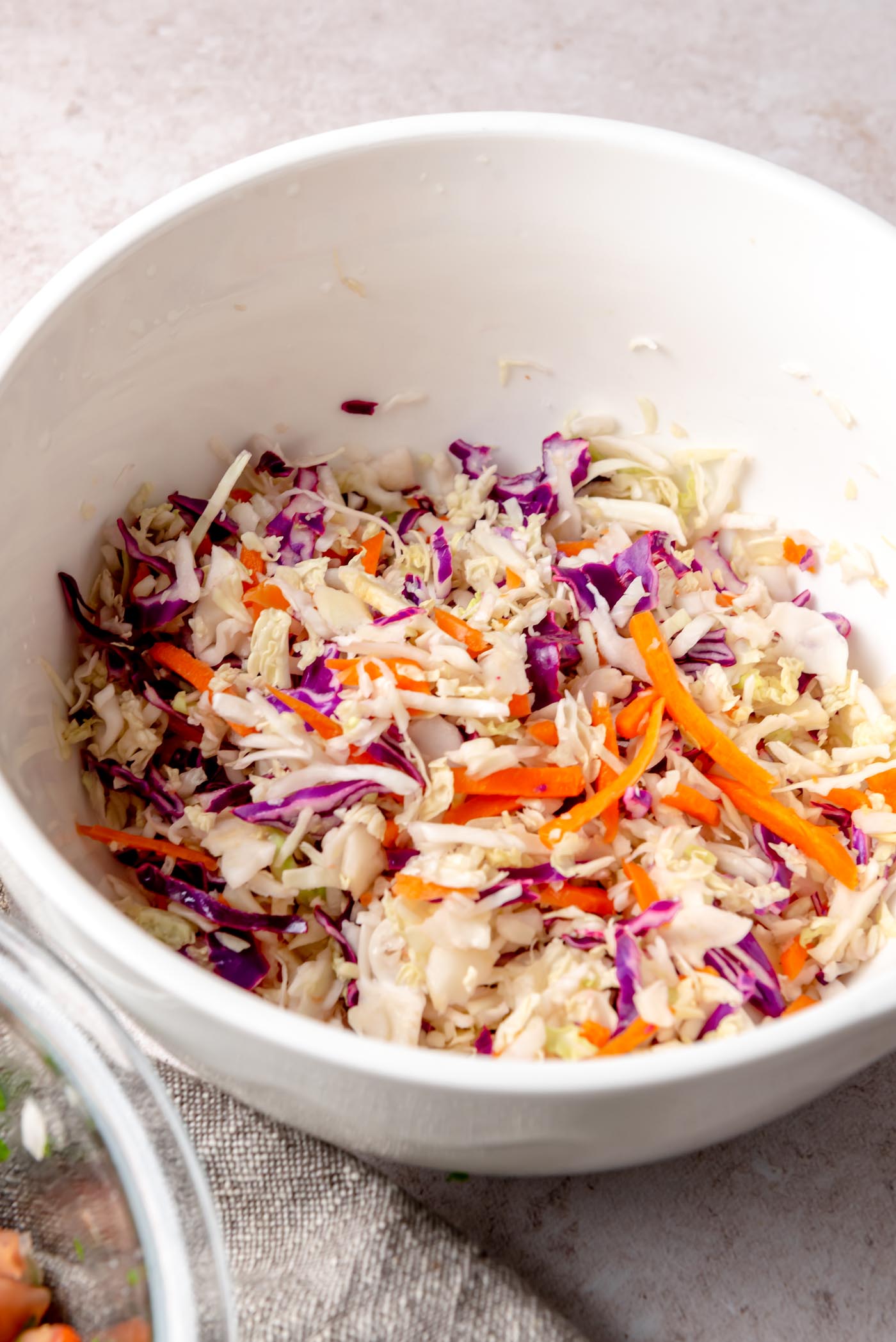 Shredded cabbage slaw with carrots and purple cabbage in a white mixing bowl.