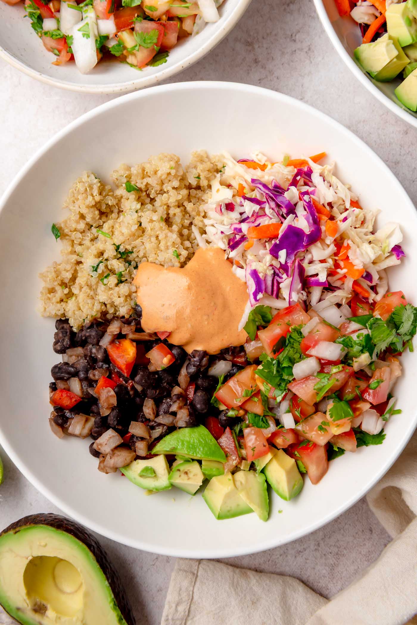 A vegan burrito bowl with quinoa, black beans, cabbage slaw, pico de gallo, avocado, and chipotle sauce.