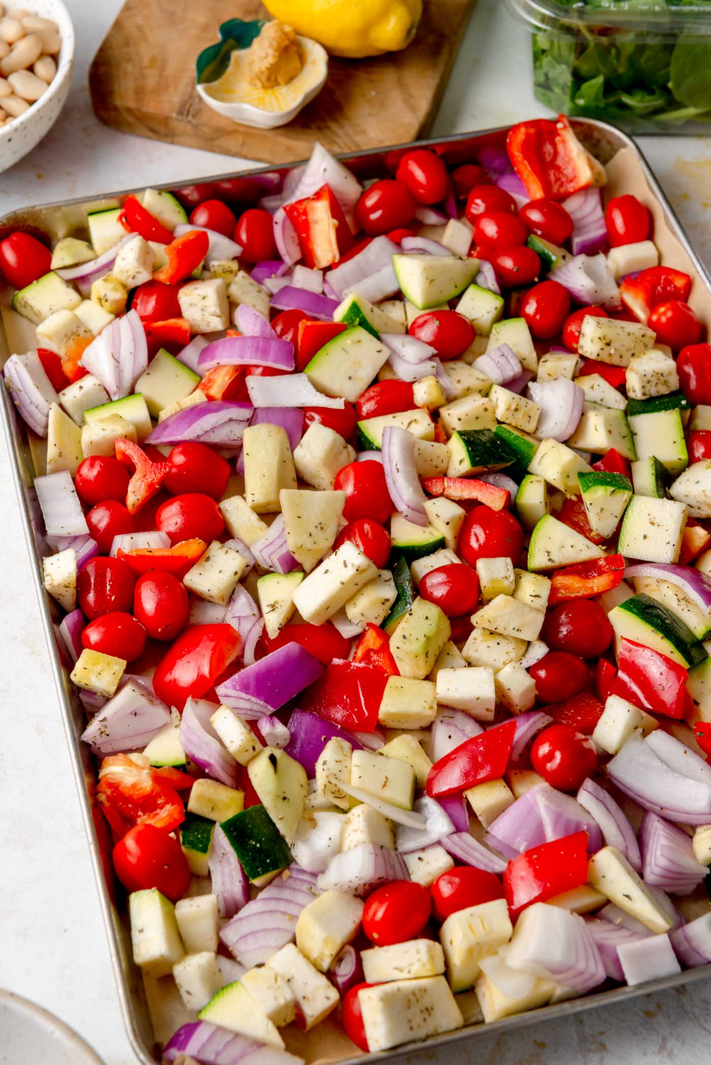 Chopped zucchini, eggplant, red onion, red pepper, and cherry tomatoes tossed with herbs and spread across a sheet pan before roasting.