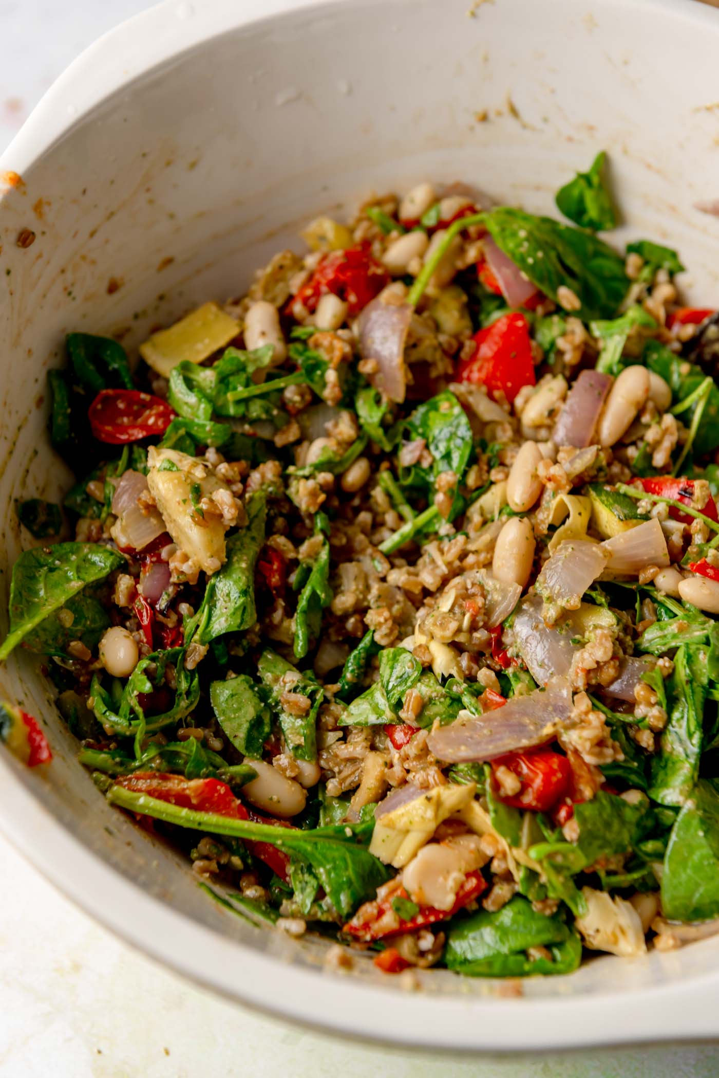A large bowl of warm farro salad mixed with roasted vegetables, white beans, greens, and pesto.
