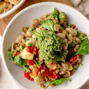 A serving bowl filled with warm pesto farro salad topped with a generous spoonful of green pesto.