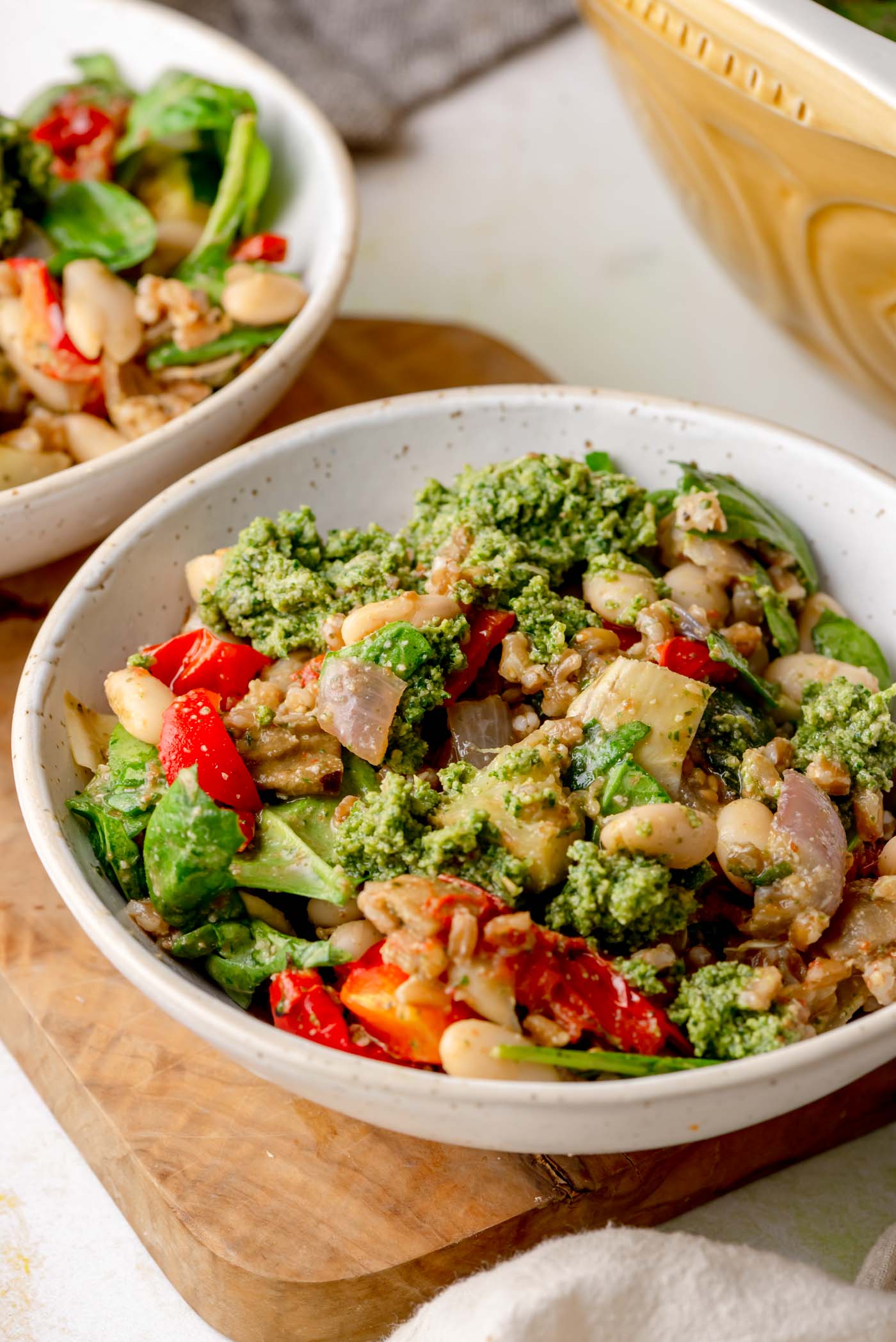 Two bowls of warm pesto farro salad with white beans, roasted vegetables, greens, and dollops of pesto.