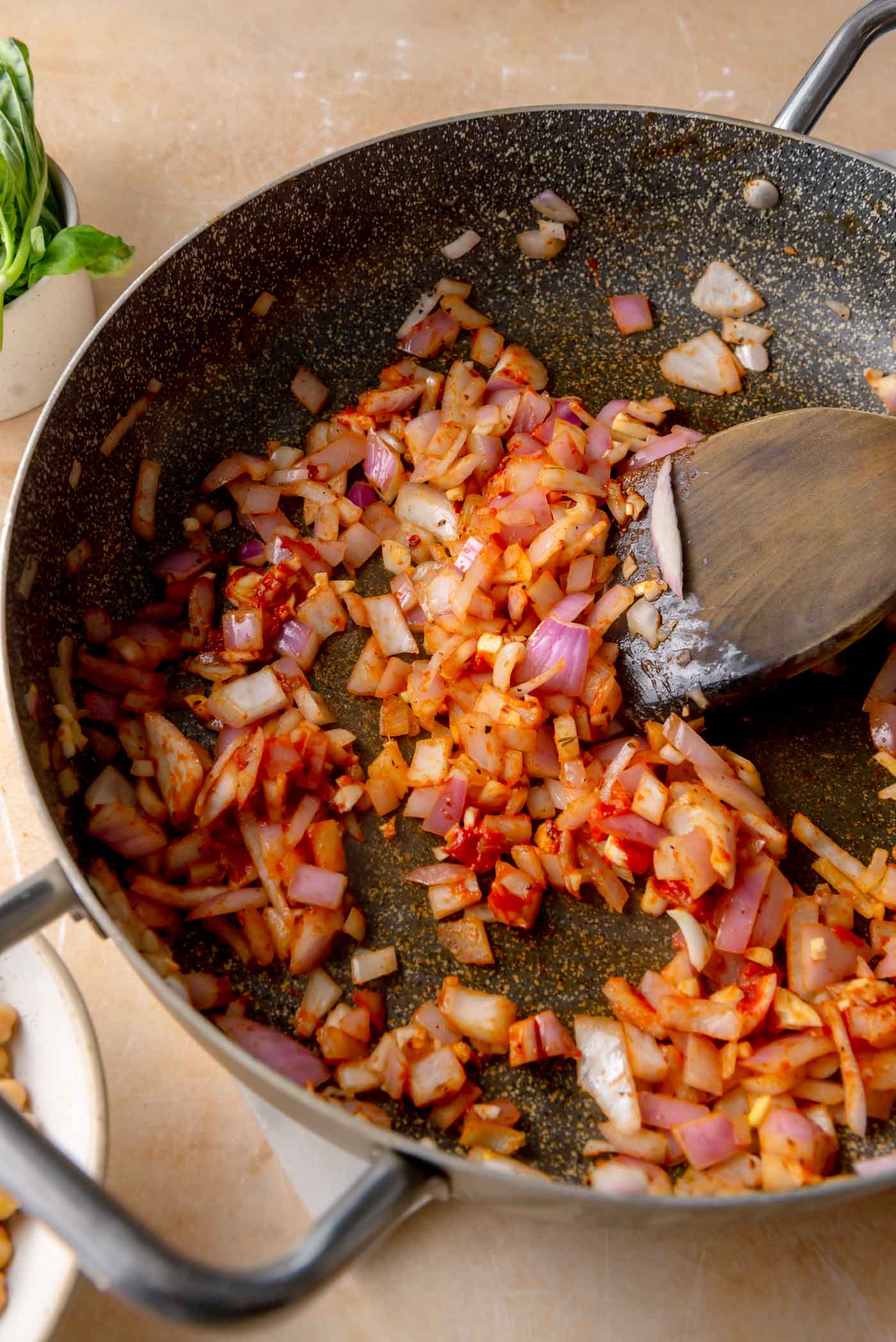 Softened red onion cooking in a skillet with minced garlic, red chili flakes, and tomato paste, creating a deep red, fragrant base for the sauce.