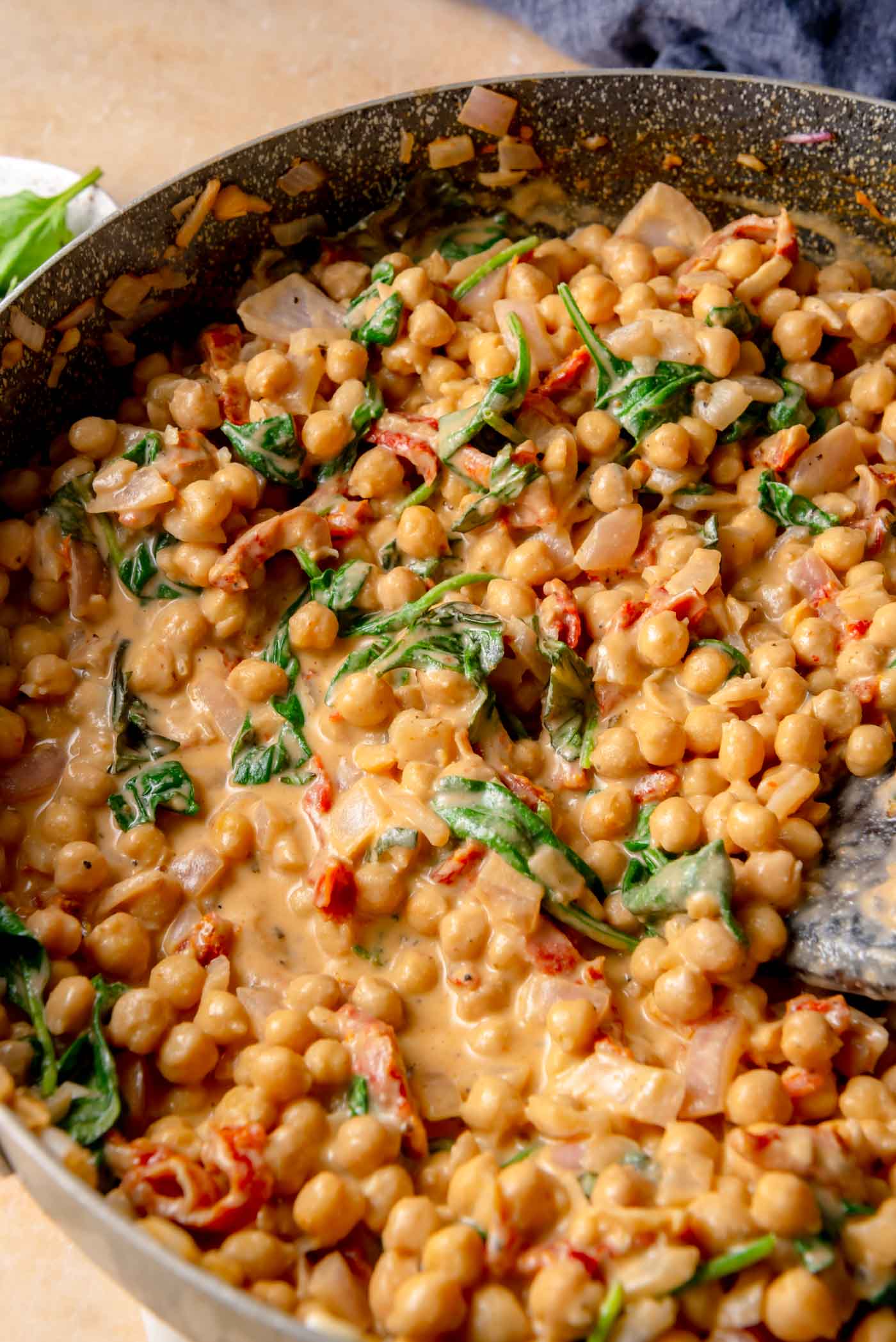 Creamy chickpea sauce simmering in a skillet with sun-dried tomatoes and wilted spinach, showing a thick, glossy texture.