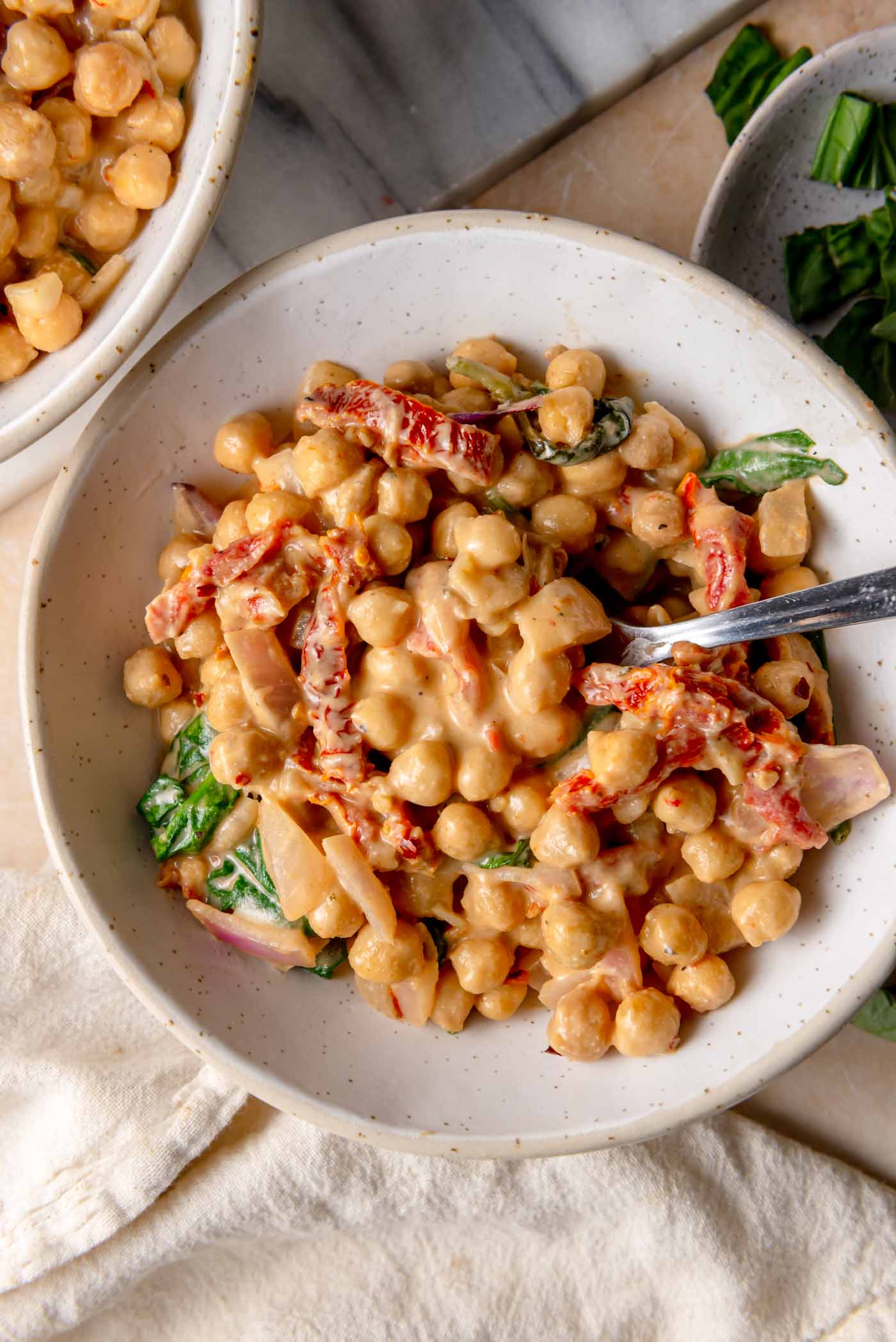 White bowl filled with creamy “marry me” chickpeas, coated in a rich cashew-based sauce with sun-dried tomatoes and spinach, ready to serve.