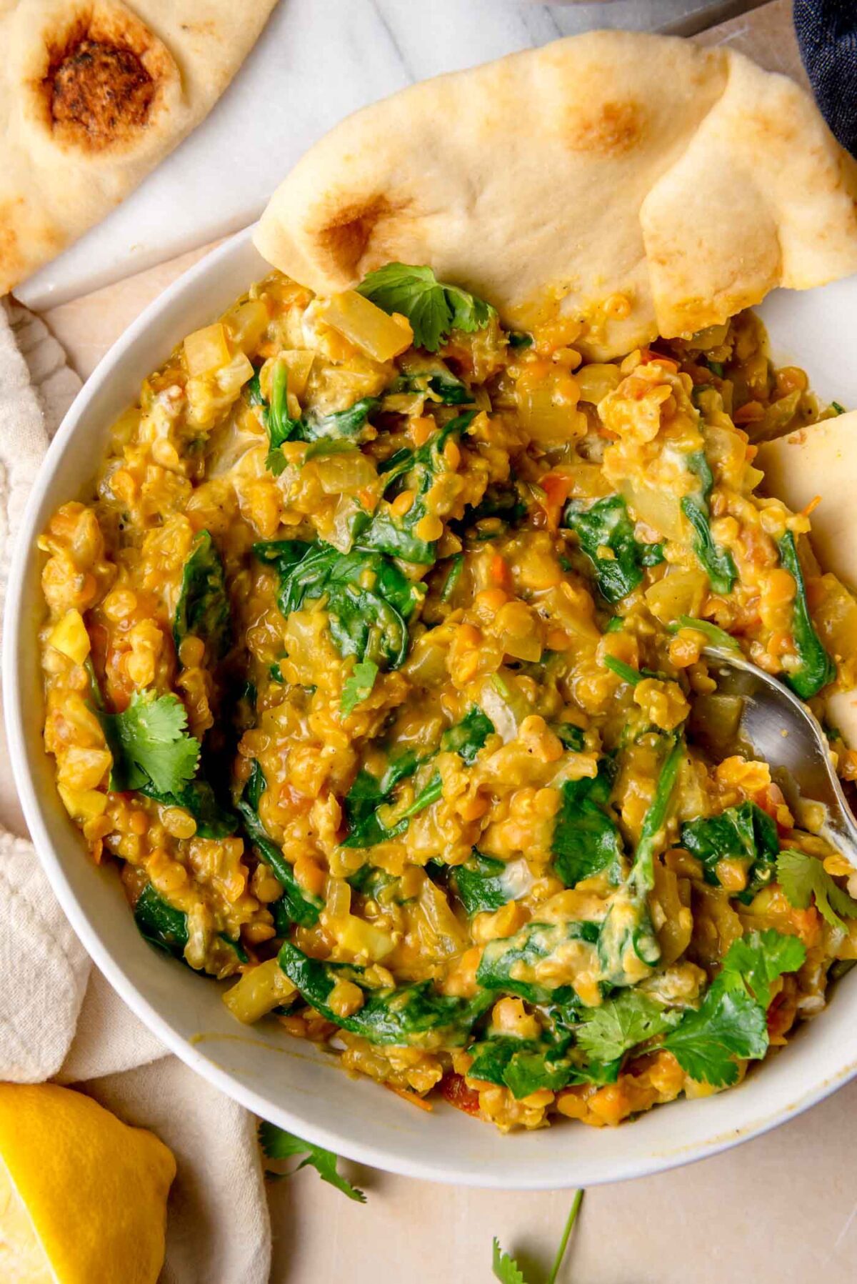Overhead view of a bowl of spinach and red lentil curry with naan bread.