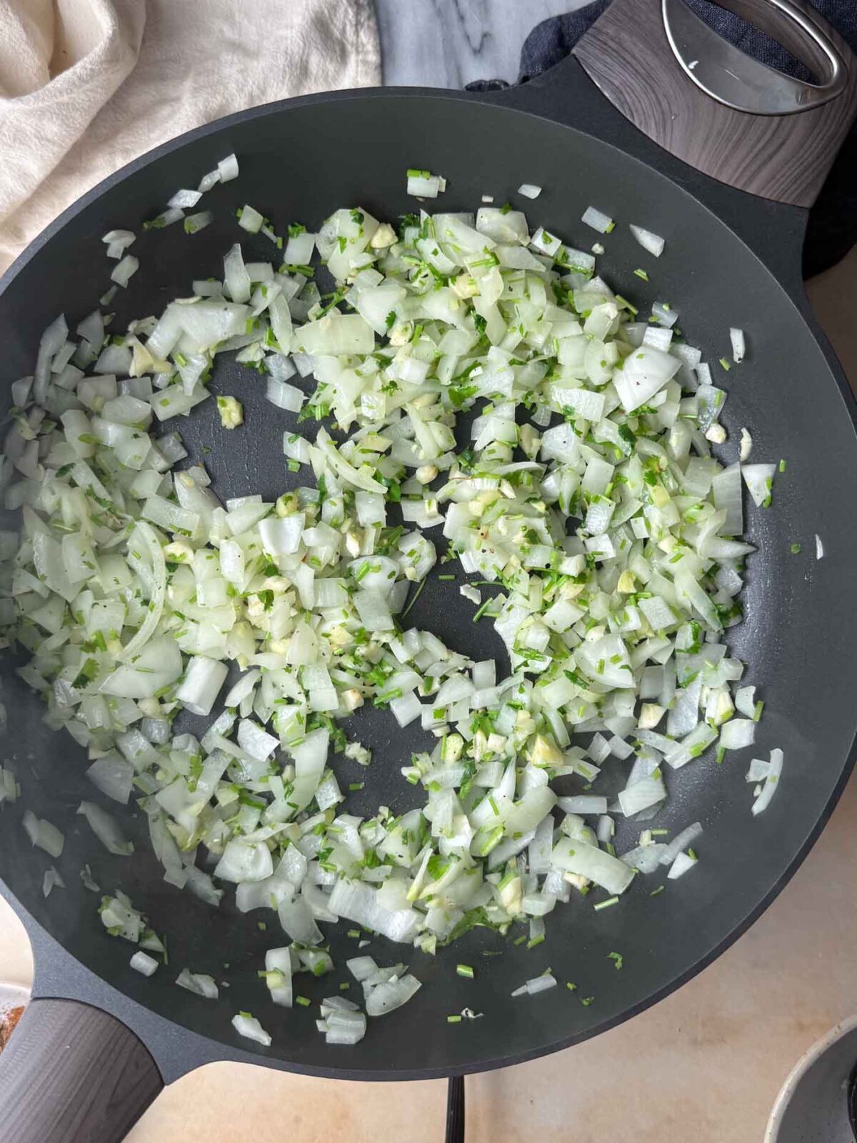 Diced onion cooking with garlic and fresh herbs in a skillet.