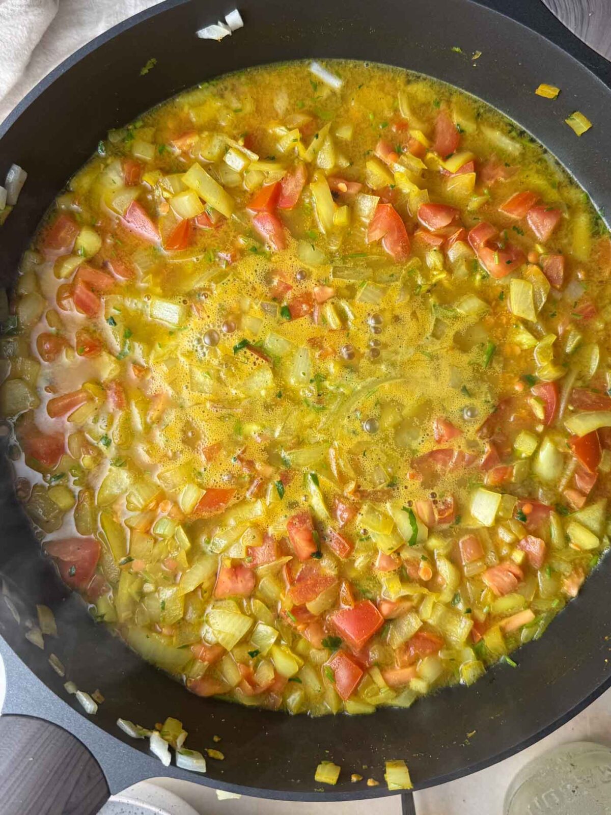 Onion and tomato mixture covered with golden-colored liquid in a pan.