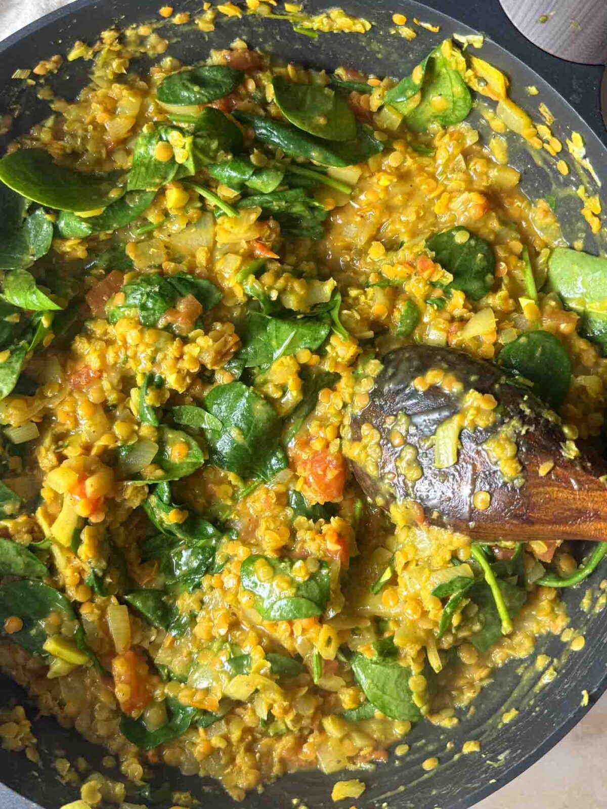 Red lentils and fresh spinach stirred into the curry mixture in a pan.