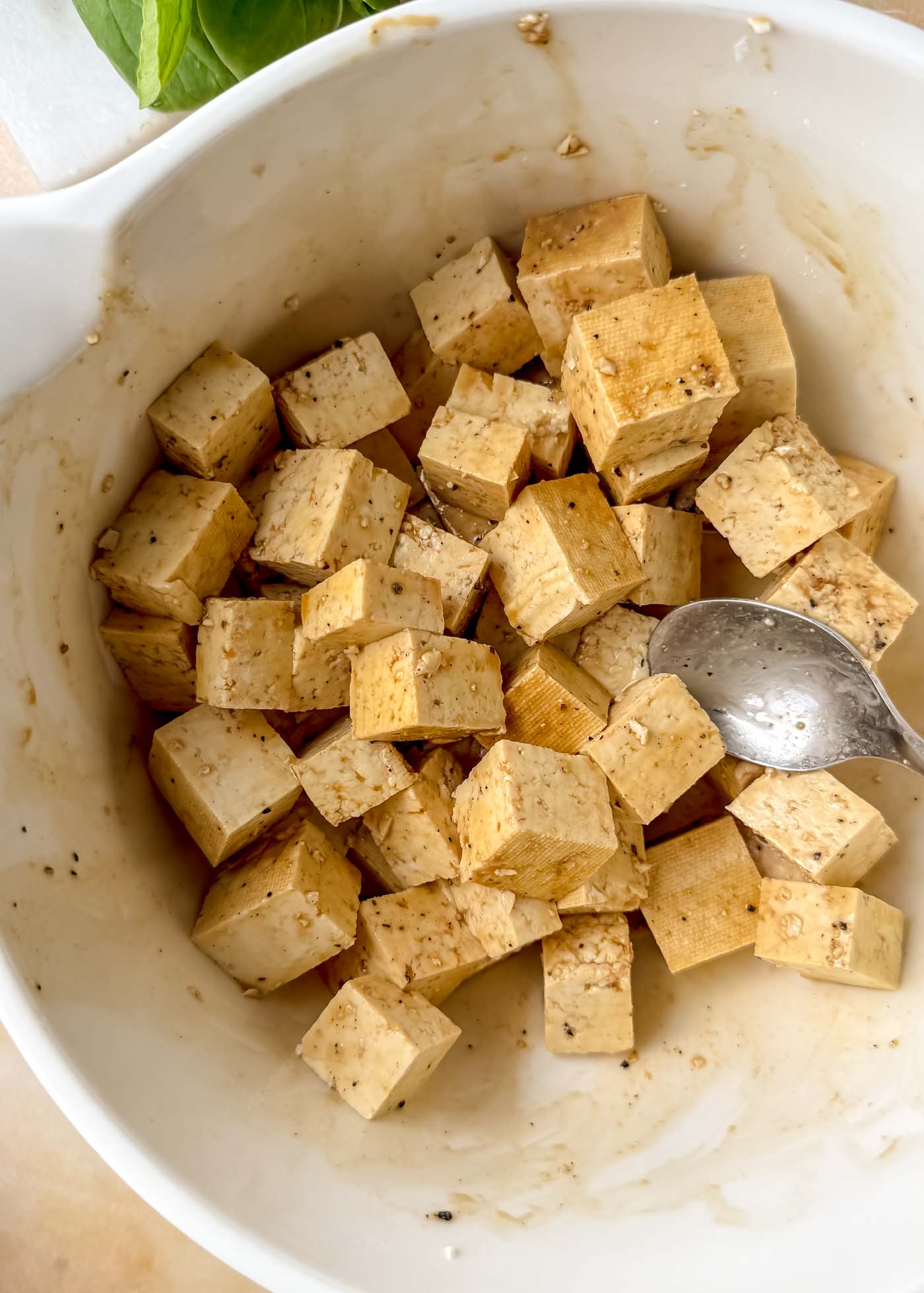 Cubed tofu coated in a light brown marinade inside a white mixing bowl before cooking.