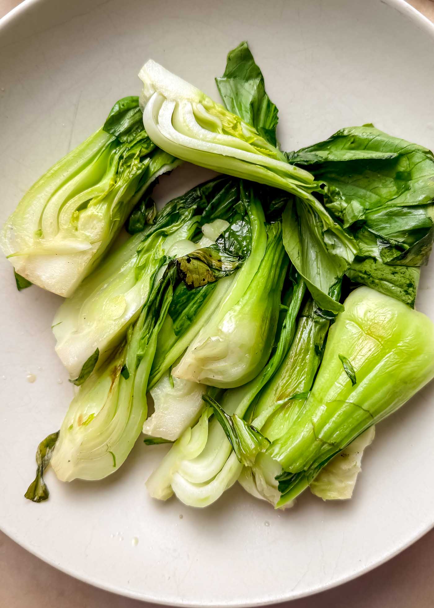 Steamed bok choy with pale green stems and dark green leaves resting on a white plate.