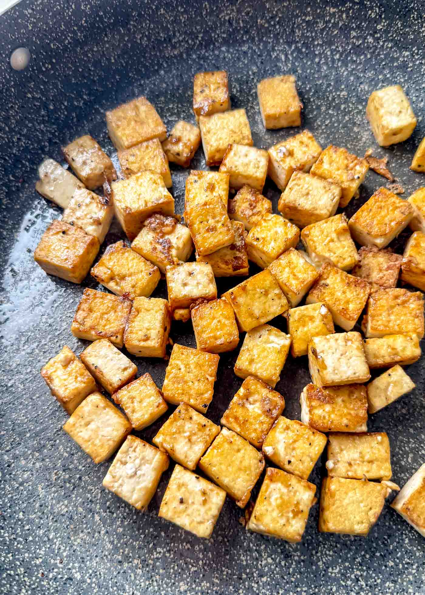 Golden, crispy tofu cubes browning in a nonstick skillet with lightly caramelized edges.
