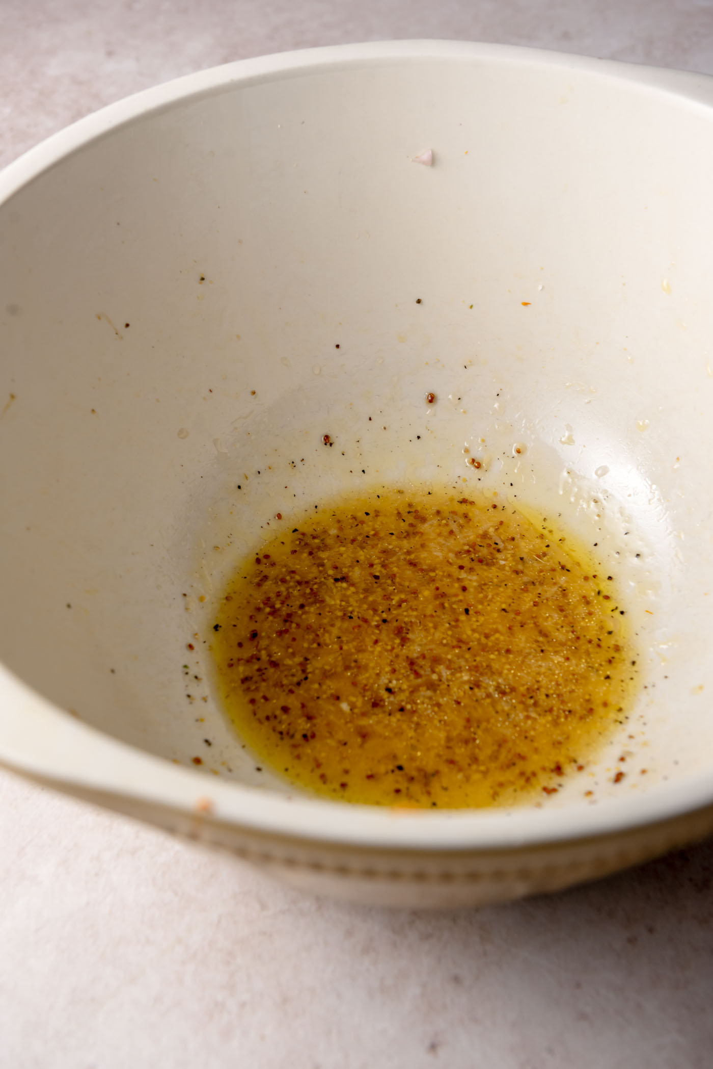 Apple cider vinaigrette with olive oil, Dijon mustard, maple syrup and spices whisked together in a white bowl.
