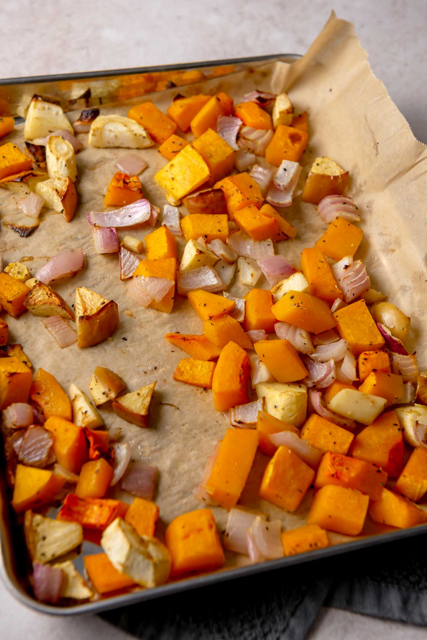 Roasted butternut squash, apples and red onion spread on a parchment-lined baking sheet, lightly caramelized.