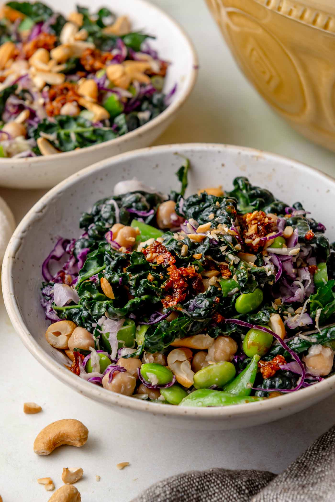 Kale miso crunch salad topped with chickpeas, edamame, snap peas, cabbage and crunchy cashews in a ceramic bowl.