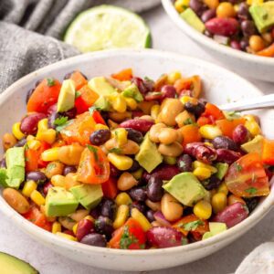 Three bean chipotle salad with corn, bell peppers, and avocado served in a white bowl with lime.