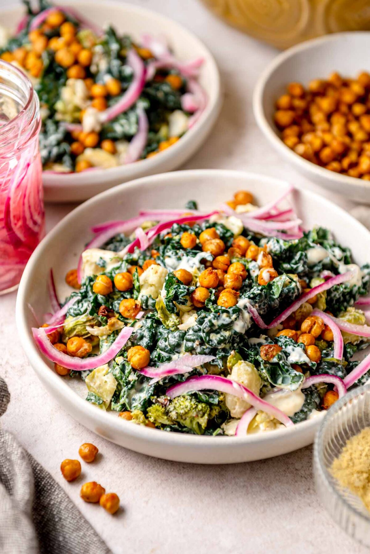 Roasted vegetable Caesar salad with crispy chickpeas, kale, broccoli, cauliflower, and pickled red onions in a creamy dressing, served in a shallow bowl.