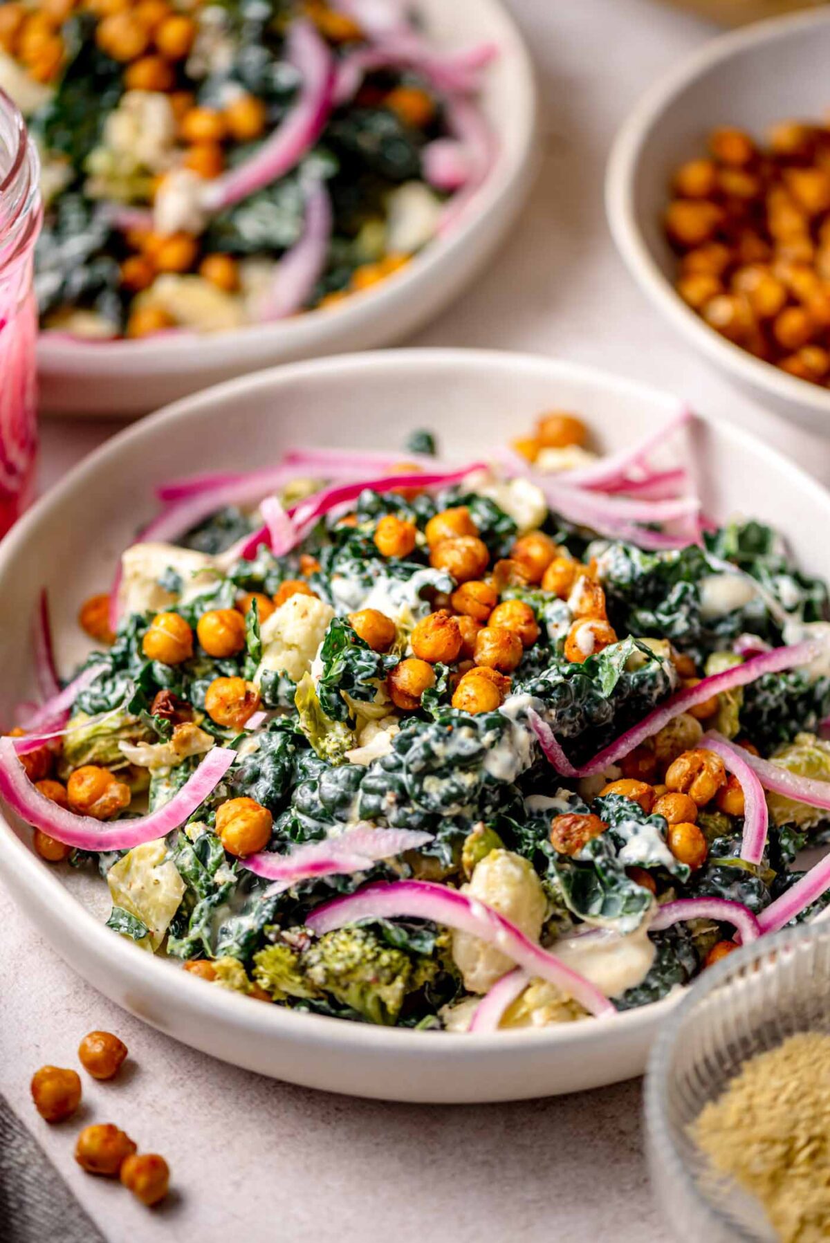 Roasted vegetable Caesar salad with crispy chickpeas, kale, broccoli, cauliflower, and pickled red onions in a creamy dressing, served in a shallow bowl.