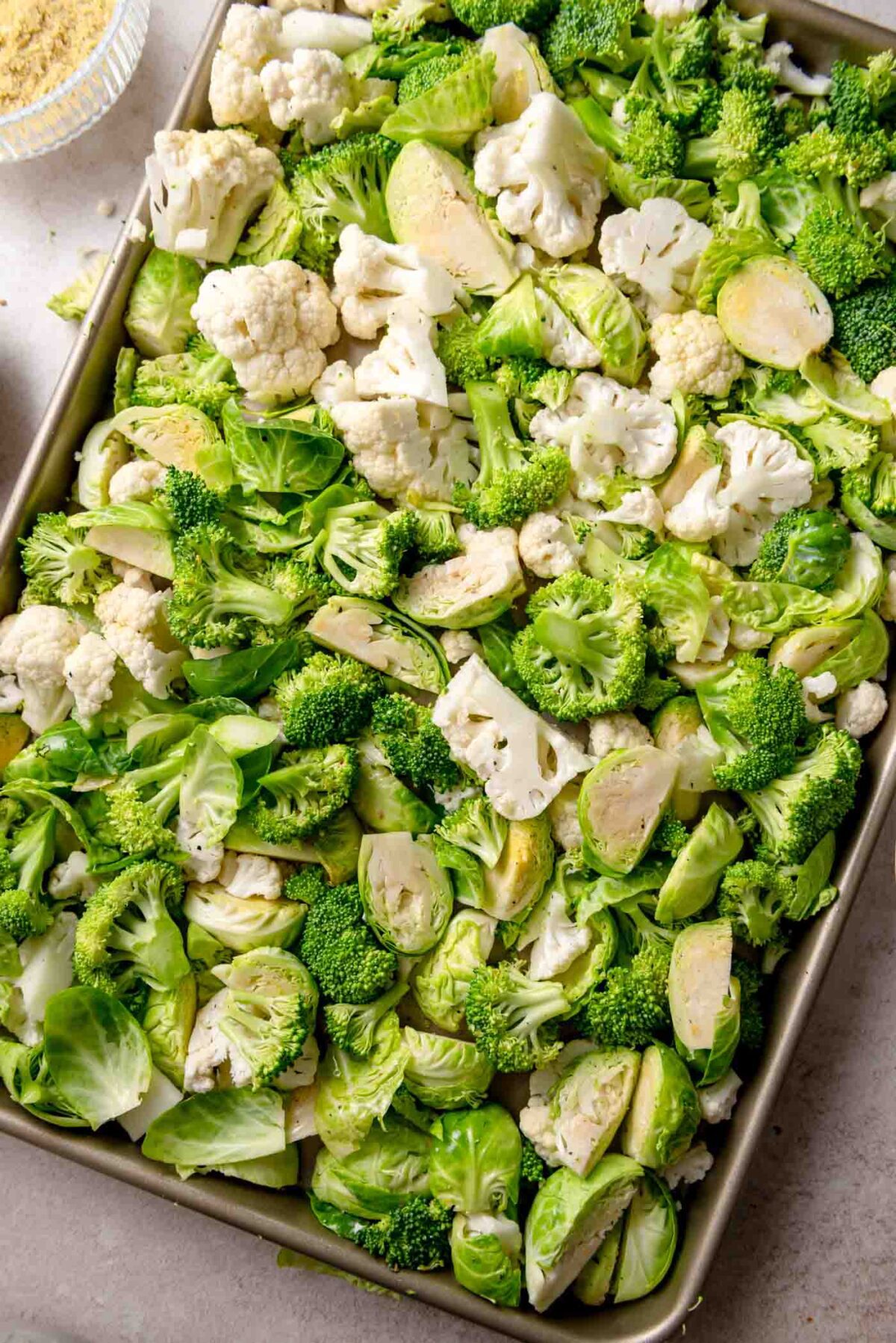 Sheet pan of raw broccoli, cauliflower, and Brussels sprouts prepared for roasting.