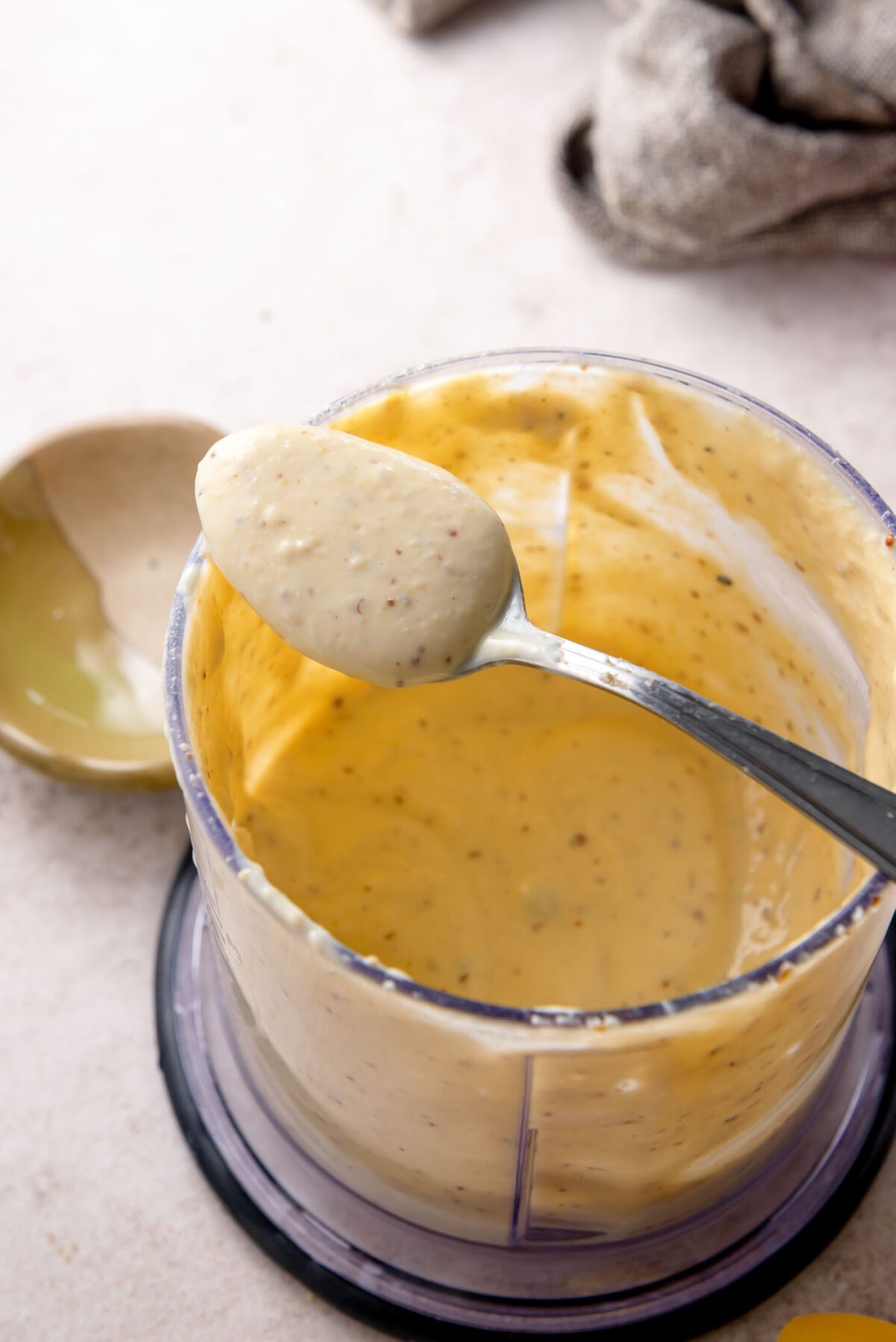 Creamy vegan Caesar dressing blended smooth in a small food processor, shown on a spoon.