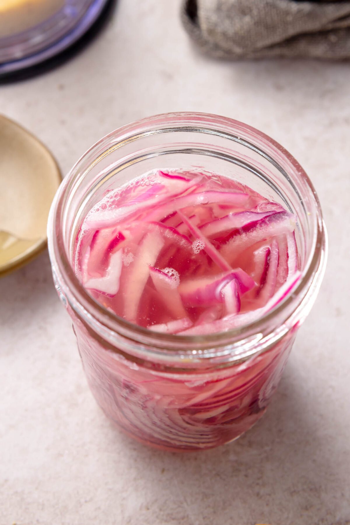 Glass jar filled with quick-pickled red onions in pink brine.